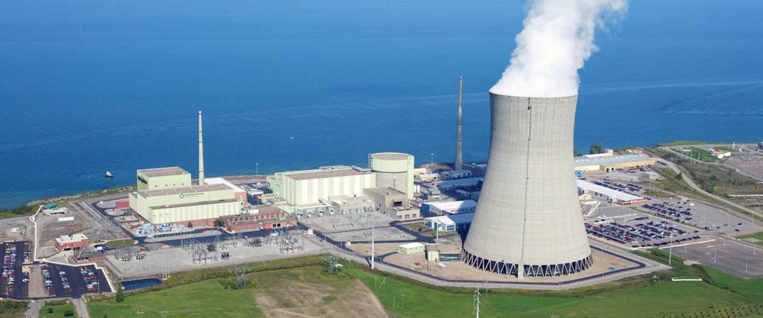 A nuclear power plant with the nuclear plant (small rectangle buildings and one cylindrical building) and a cooling tower (big steaming parabolic-shaped tower). Nuclear power plants never shut down, except to change fuel rods. 